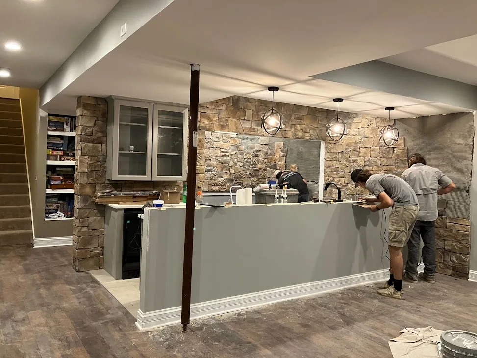 Basement bar renovation in progress with a stone wall and crew at work