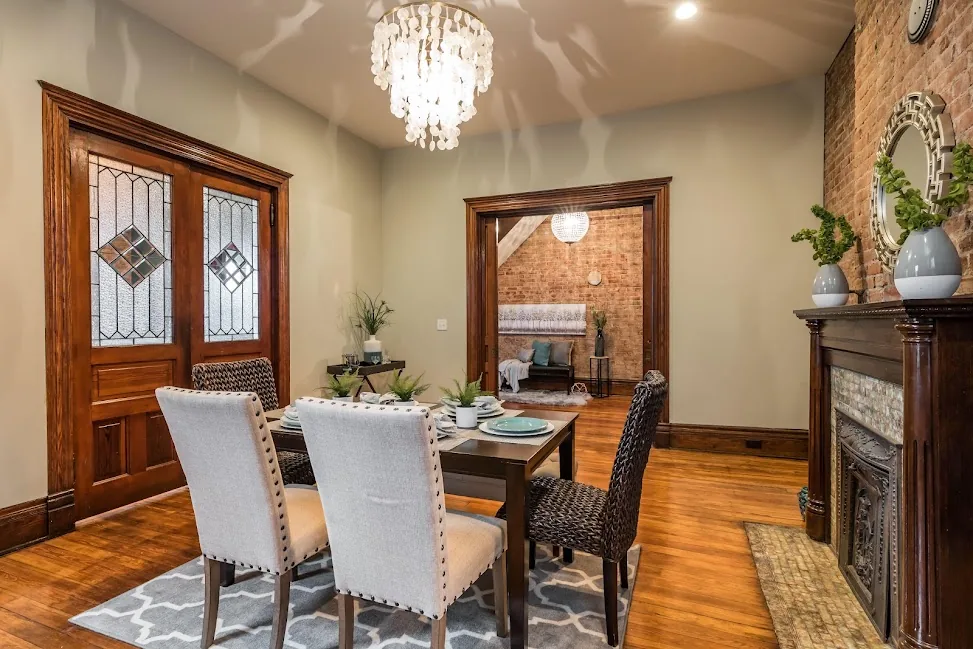 Renovated dining room with a brick fireplace, wood floors, and chandelier